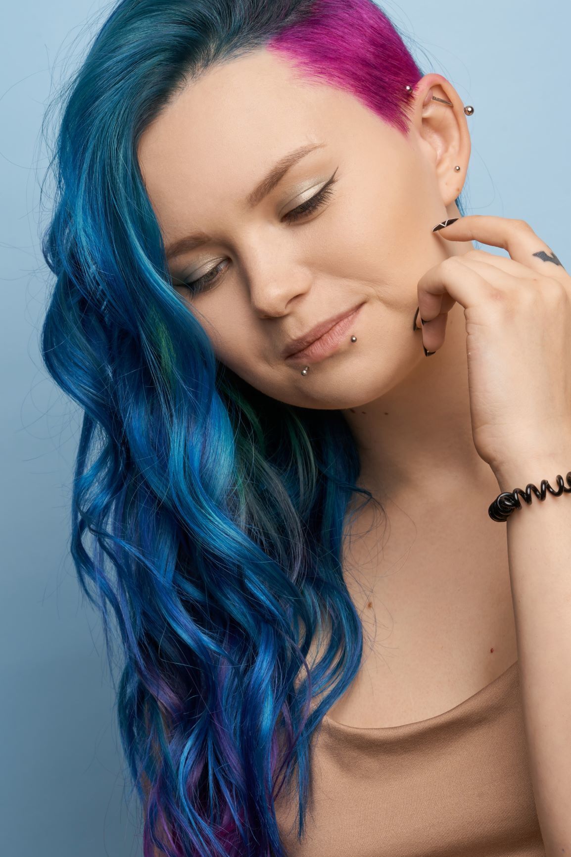 Mulher de cabelos longos pintados de azul e lateral raspada pintada de roxo olhando para baixo