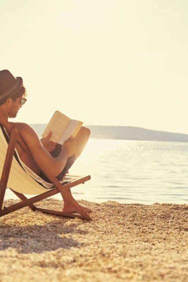 Homem lê livro e usa boné, um cuidado com o cabelo masculino na praia