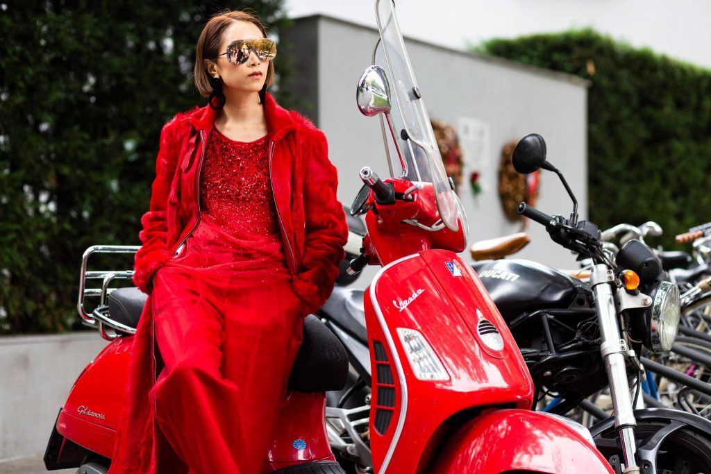 Mulher de cabelo curto e óculos escuros posa para foto sentada em moto vespa vermelha
