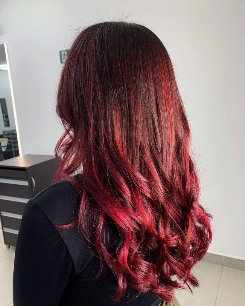 Mulher posa de costas com cabelo longo e ruivo com balaiagem