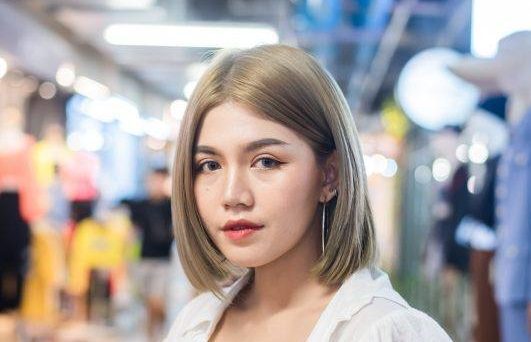 Mulher posa em espaço comercial com cabelo chanel castanho claro vestindo blusa preta e camisa branca