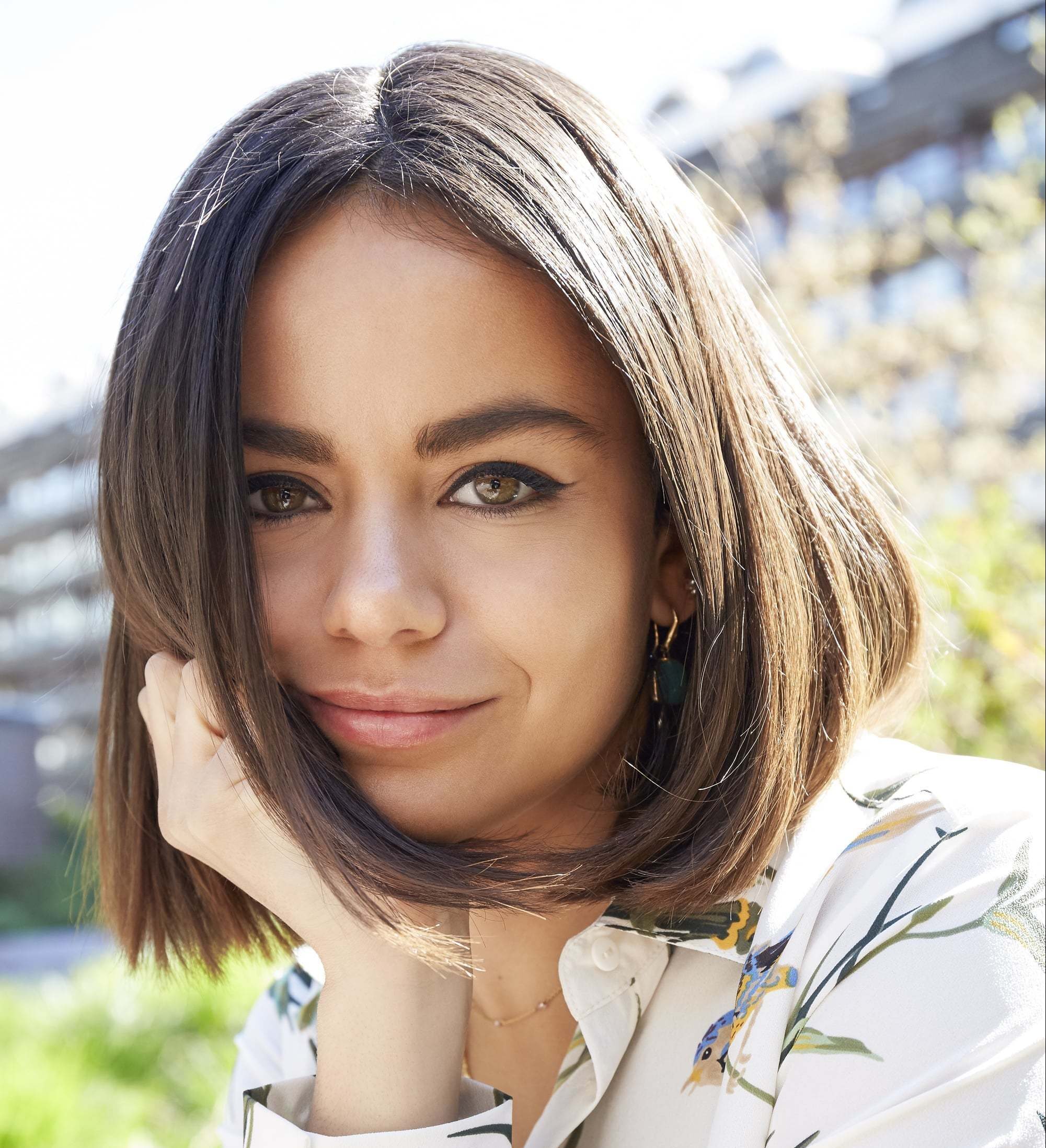 Mulher posa ao ar livre com a mão no queixo e cabelo castanho claro chanel