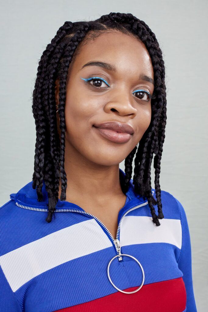 Mulher posa de jaqueta azul e tranças box braids estilo skatista no cabelo crespo ou cacheado preto