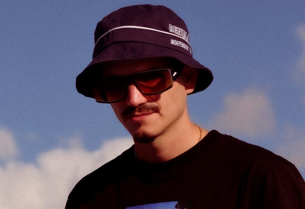 Homem posa de óculos escuros e bucket hat com cabelo estilo skatista