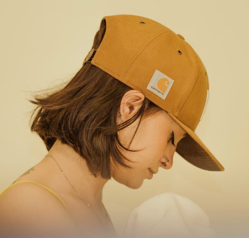 Mulher posa de perfil com cabelo curto e boné amarelo estilo skatista