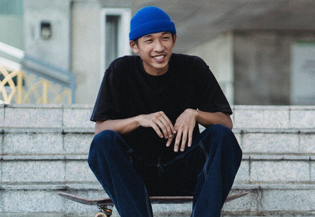 Homem posa de blusa preta e gorro azul no cabelo tipo skatista