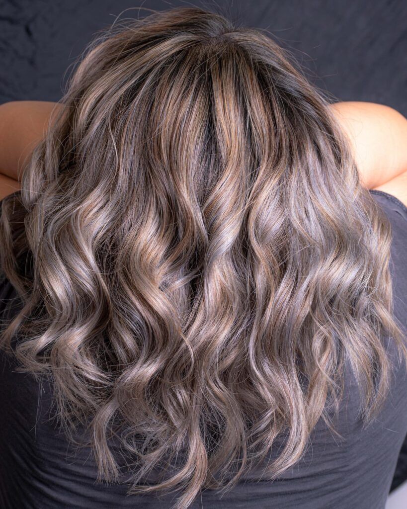 Mulher de costas segurando o cabelo médio loiro escuro acinzentado com babyliss