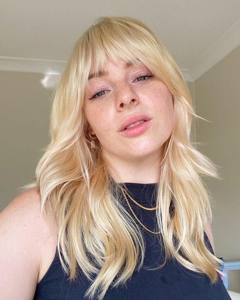 Mulher com cabelo loiro platinado e franja desfiada