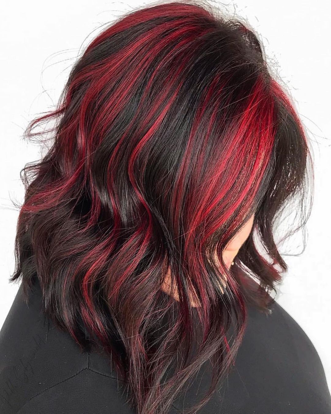 mulher com cabelo desfiado preto pintado com mechas vermelhas olhando para baixo