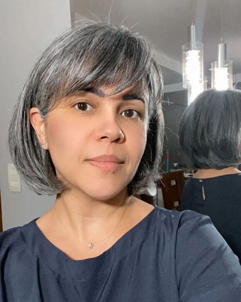 Mulher posa com blusa azul escura e cabelo grisalho com corte french bob e franja lateral