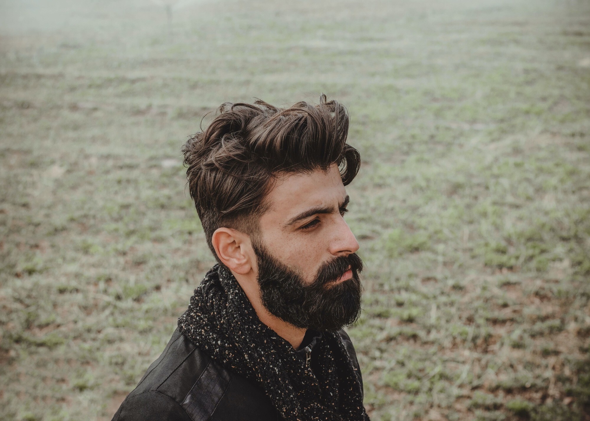 Homem de cabelo curto castanho volumoso posa ao ar livre com roupas de frio
