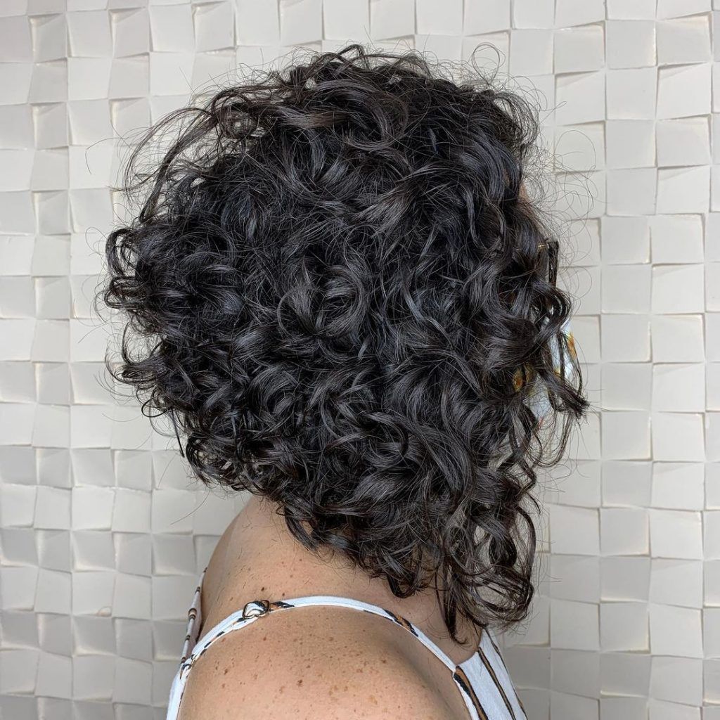 Mulher posa de lado destacando o corte de cabelo chanel de bico nos fios cacheados 3a pretos
