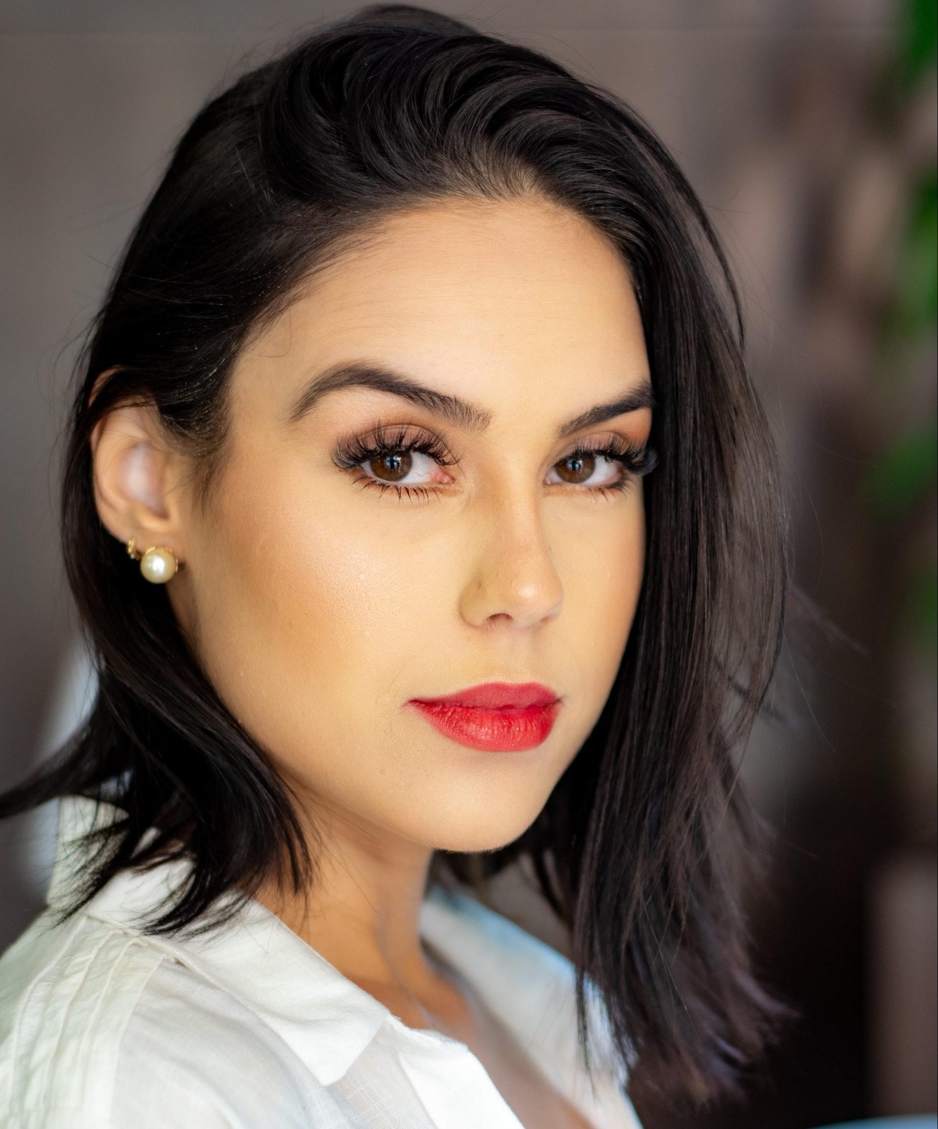 Mulher posa de perfil com camisa branca e corte de cabelo chanel de bico no cabelo castanho