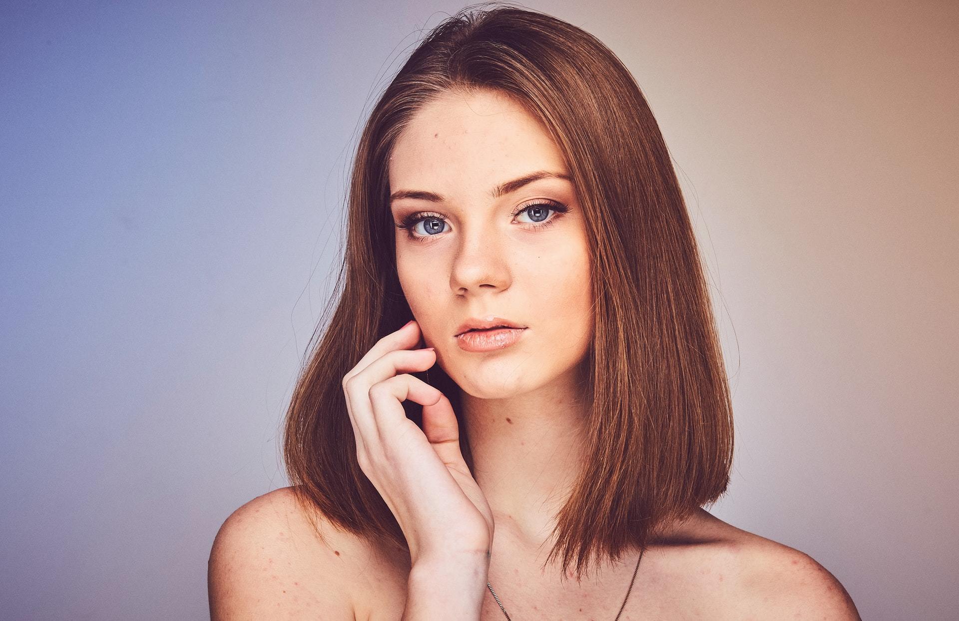mulher com cabelo castanho posa com a mão no queixo