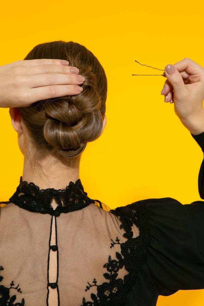  cabelo liso com coque vertical trançado sendo preso com grampo
