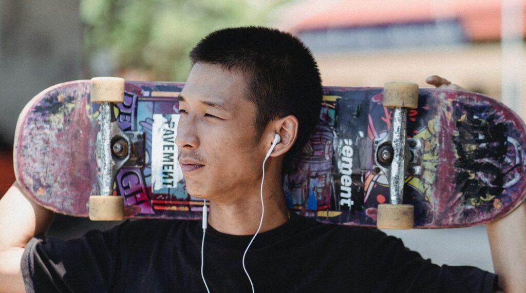 Homem posa de camiseta preta, fones de ouvido e cabelo curto raspado estilo skatista