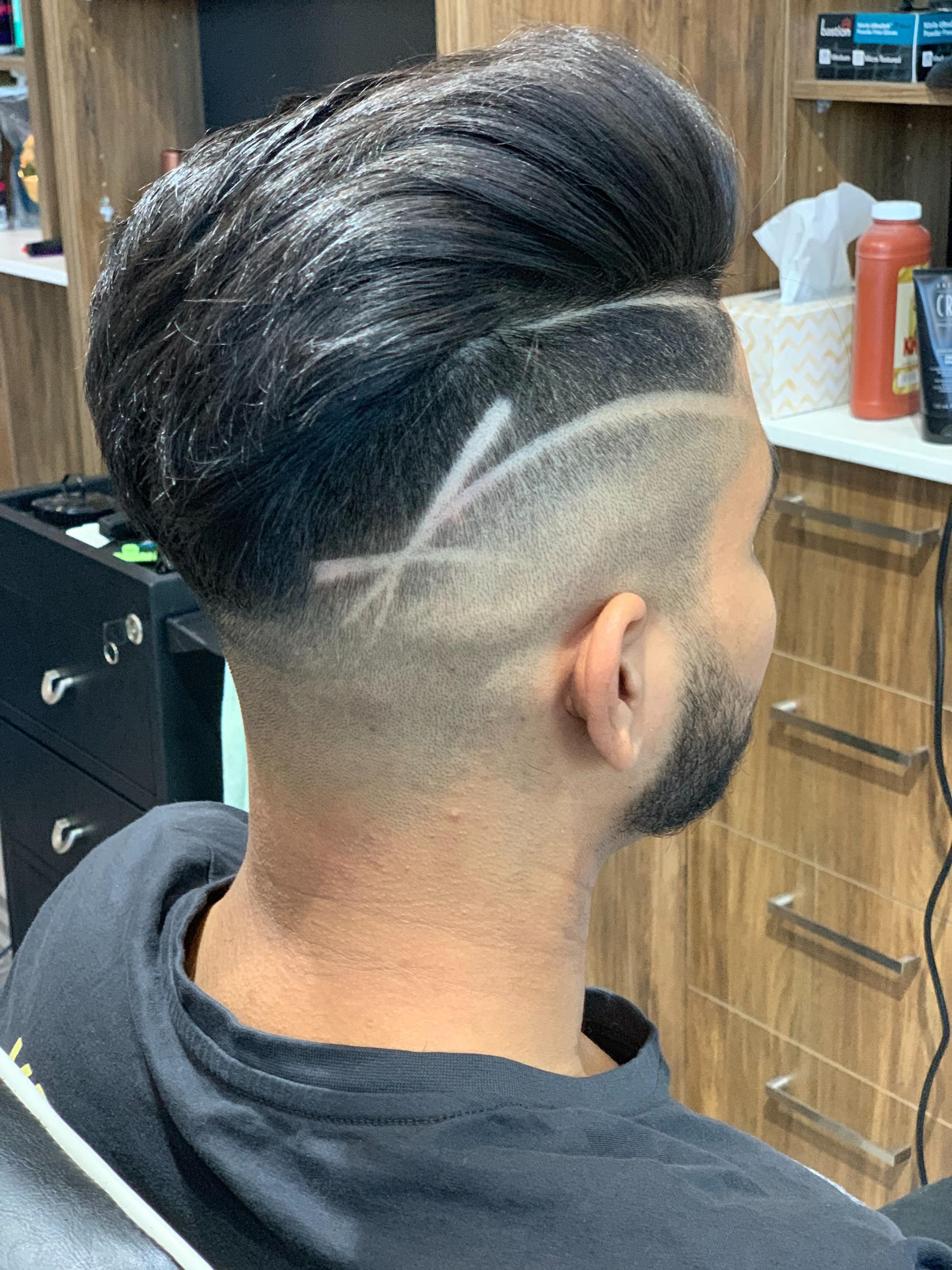 homem posa de costas no cabeleireiro mostrando corte de cabelo undercut riscado com desenho