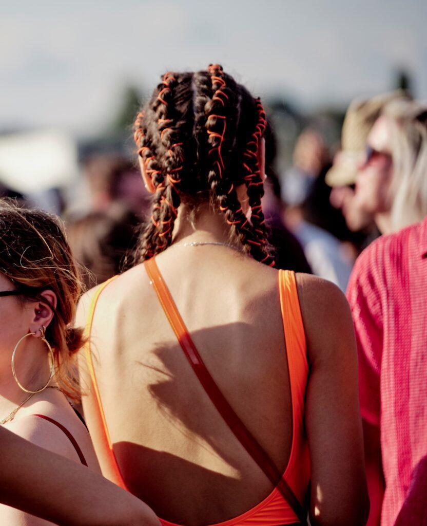 Mulher de costas com blusa laranja e trança com fita laranja posa em festival de música