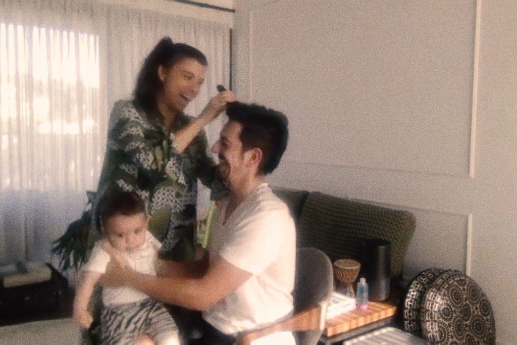 mulher sorrindo cortando cabelo de homem com bebê no colo