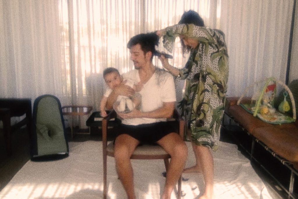 mulher cortando cabelo de homem com bebê no colo