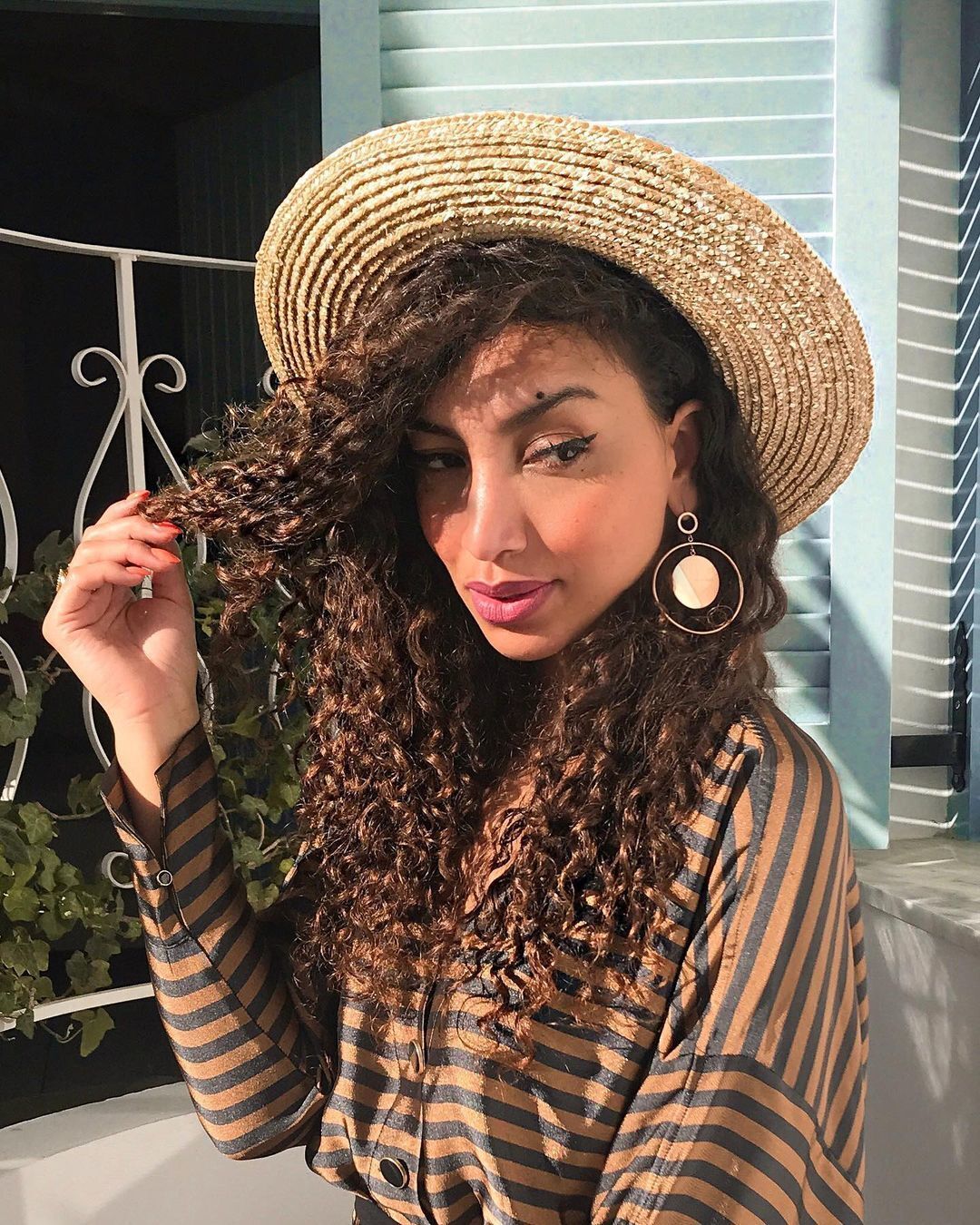 Mulher com corte de cabelo cacheado longo e chapéu na cabeça