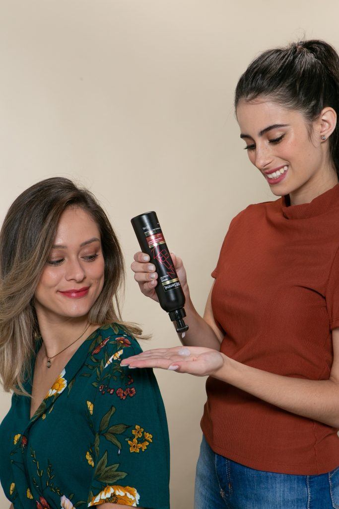 Mulher passando produto no cabelo da amiga