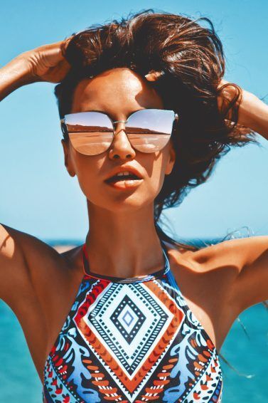 Mulher com cabelos castanhos e óculos de sol na praia