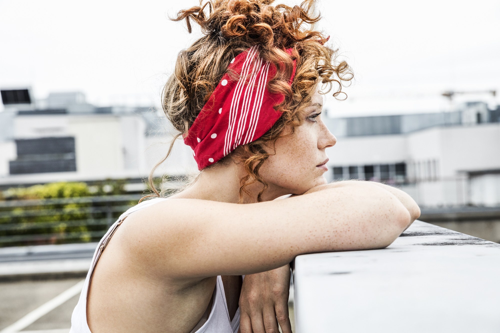 mulher encostada no muro com cabelo cacheado ruivo e bandana vermelha