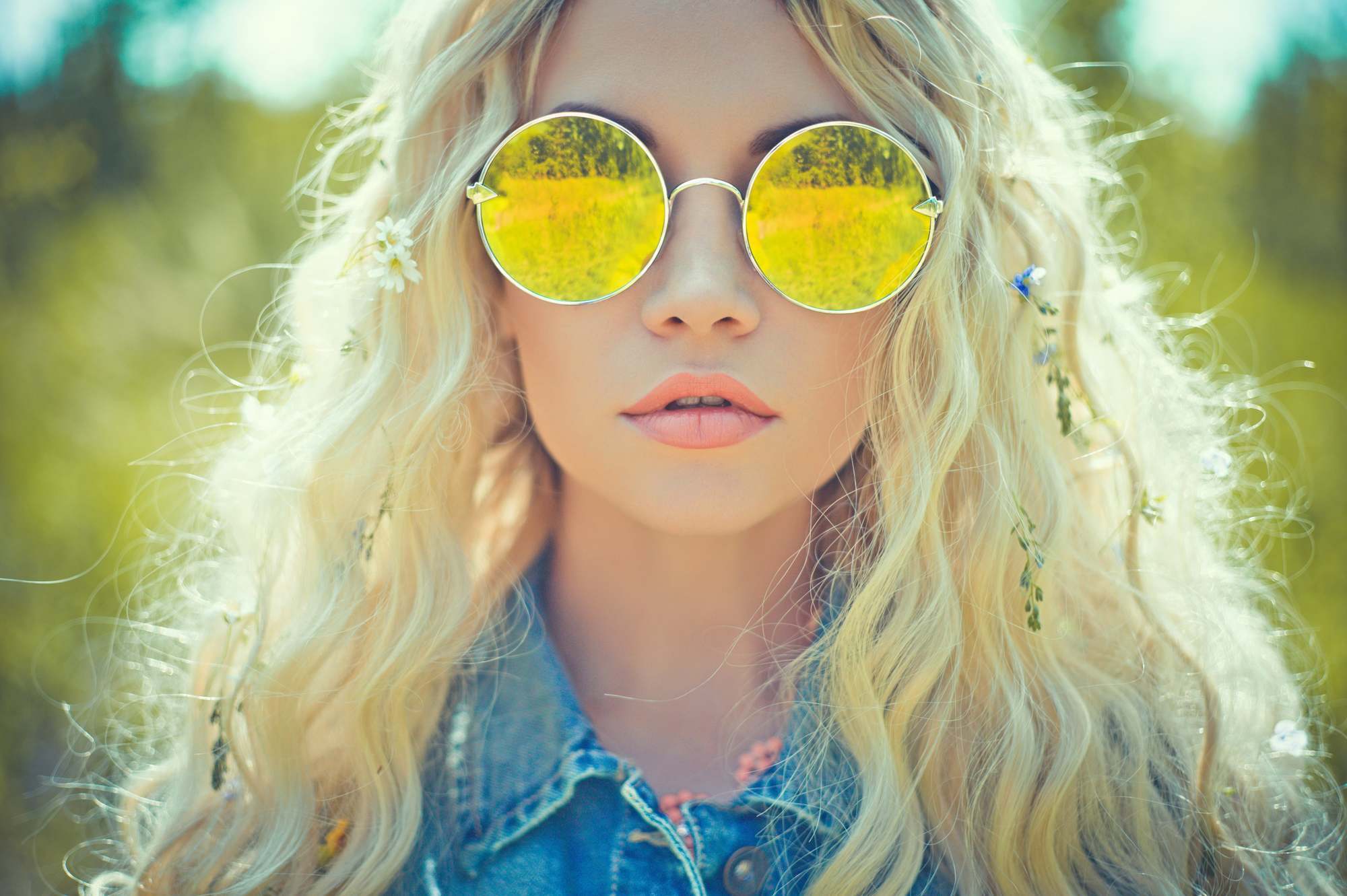 mulher loira de cabelo longo e óculos escuros de lente amarela veste camisa jeans