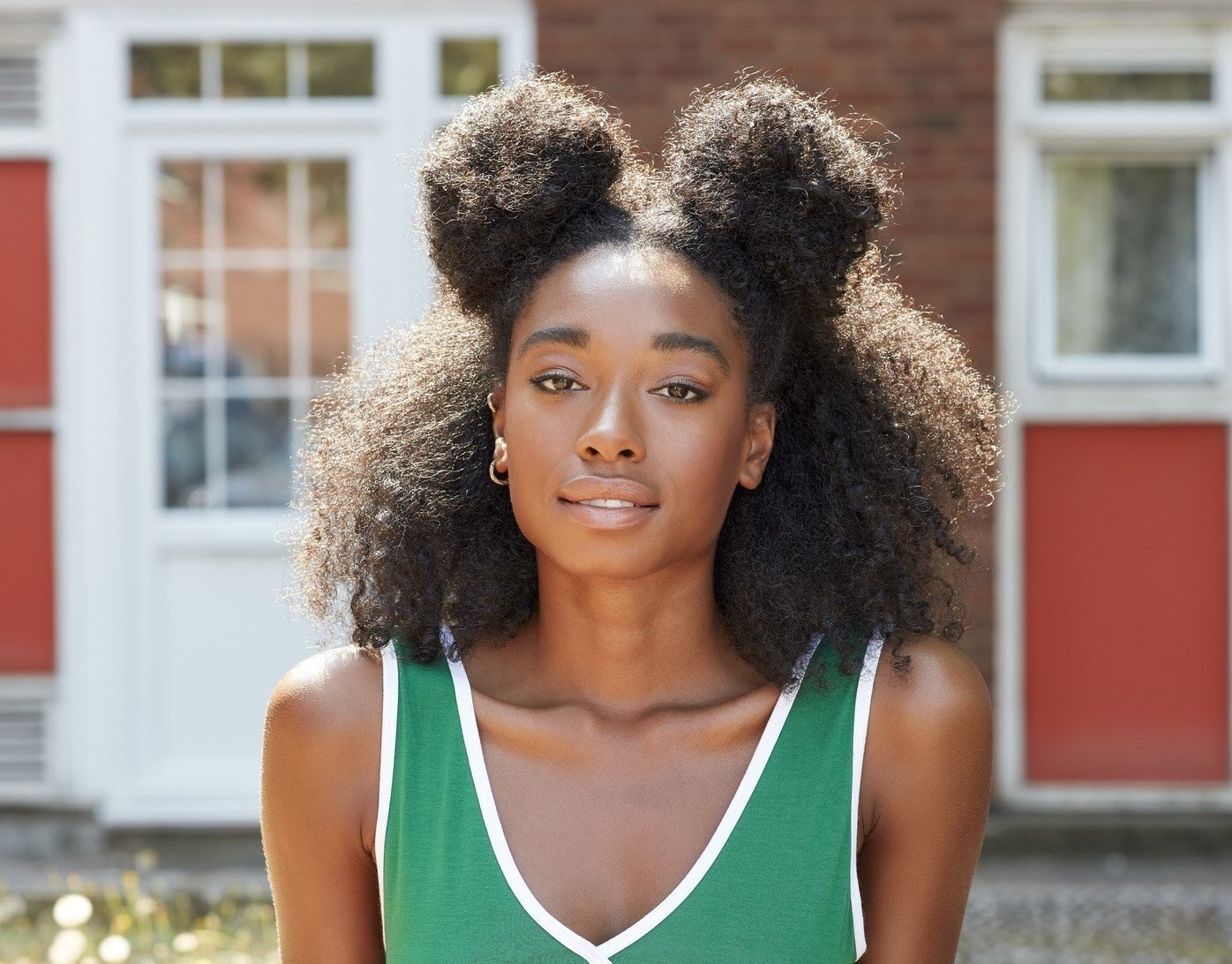 mulher com cabelo afro preto dividido em dois coques altos posa com blusa verde