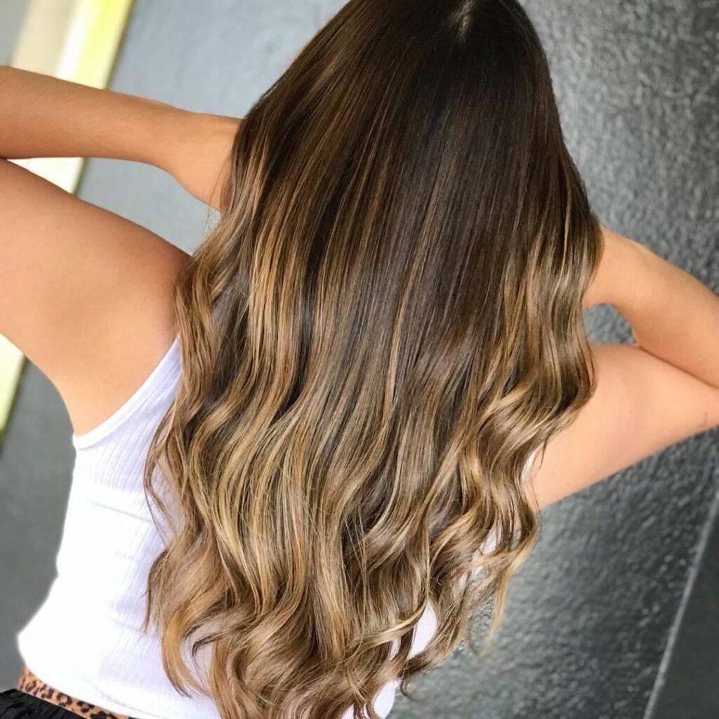 Mulher com reflexos dourados no cabelo castanho longo com ondas