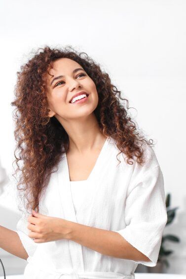 Mulher de roupão branco seca o cabelo cacheado com secador