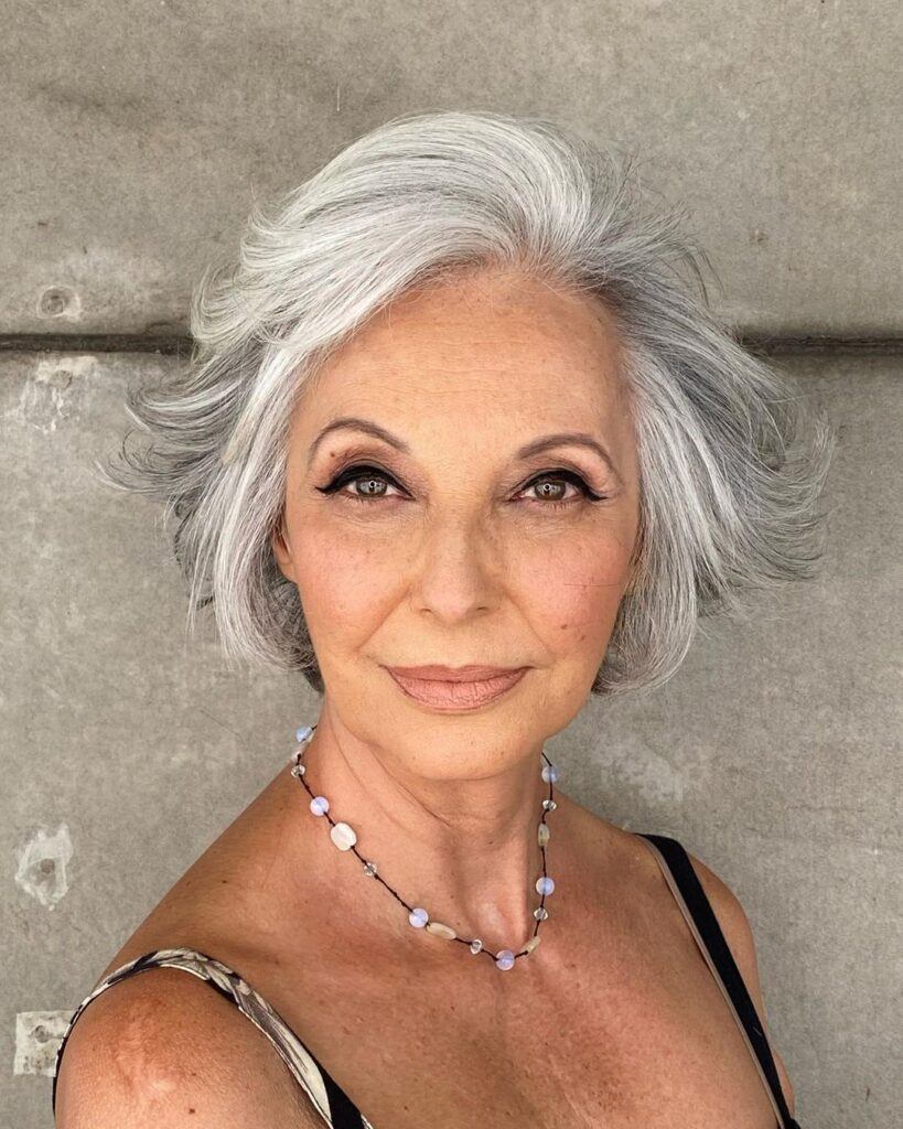 Senhora de cabelo branco posa ao ar livre com corte moderno