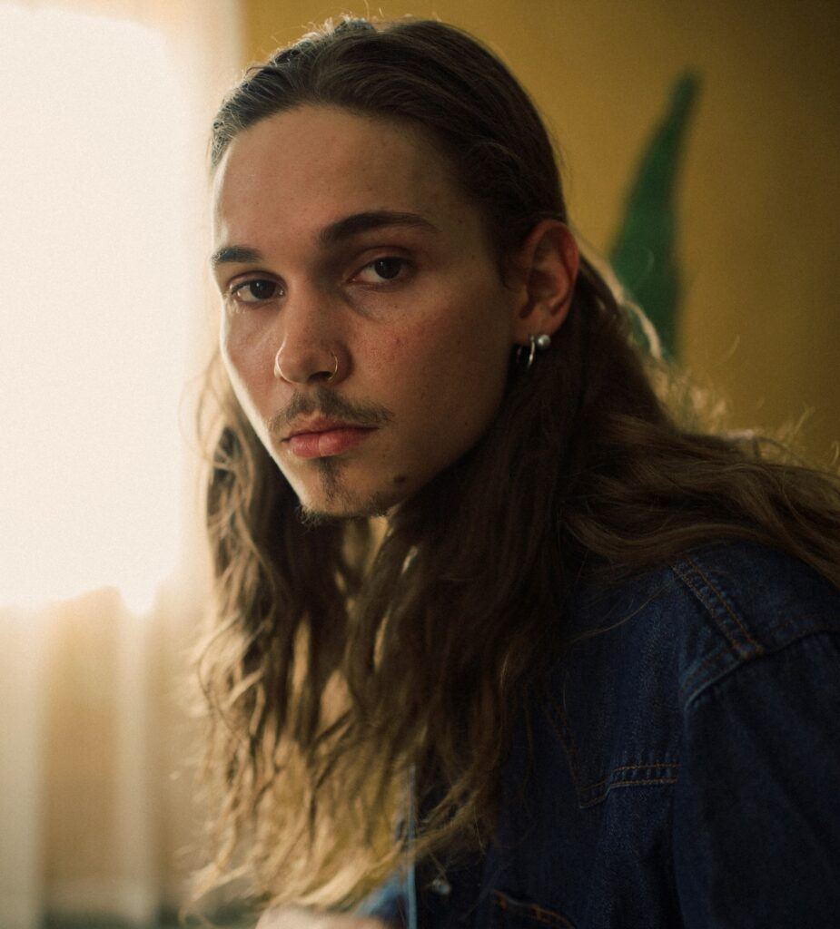 Homem posa de cabelo longo ondulado castanho estilo skatista