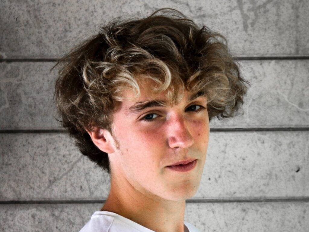 Homem posa com cabelo castanho bagunçado estilo skatista