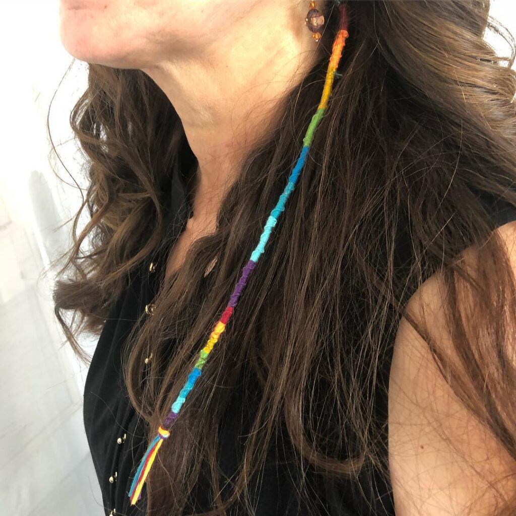 Mulher posa de blusa preta e tererê colorido no cabelo longo castanho