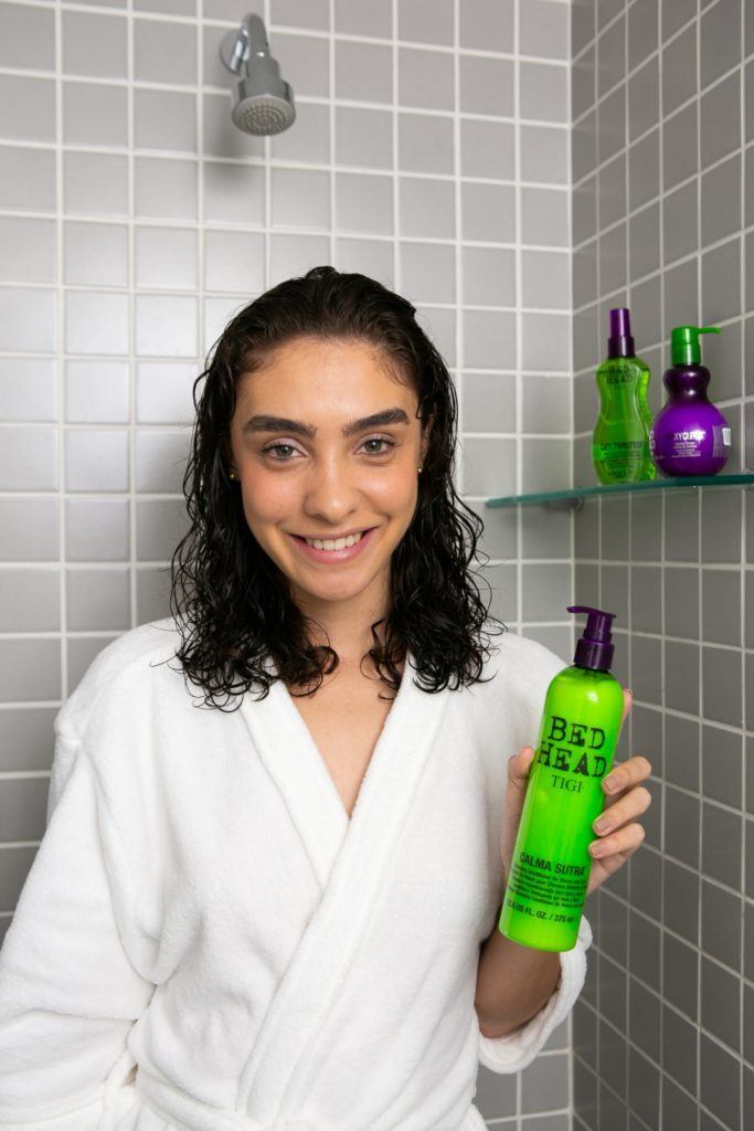 modelo no banheiro, de cabelo molhado, segura o Co Was Bed Head Calma Sutra