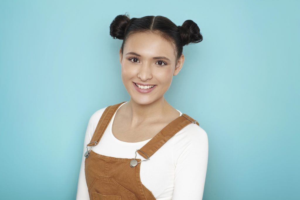 Modelo posa com space bun e veste jardineira.