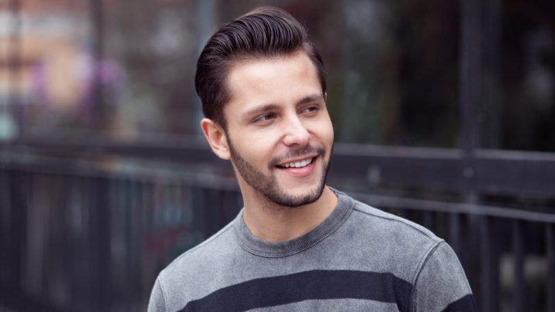 Homem usa camisa listrada cinza e preta e, no cabelo o quiff, um topete com charme discreto