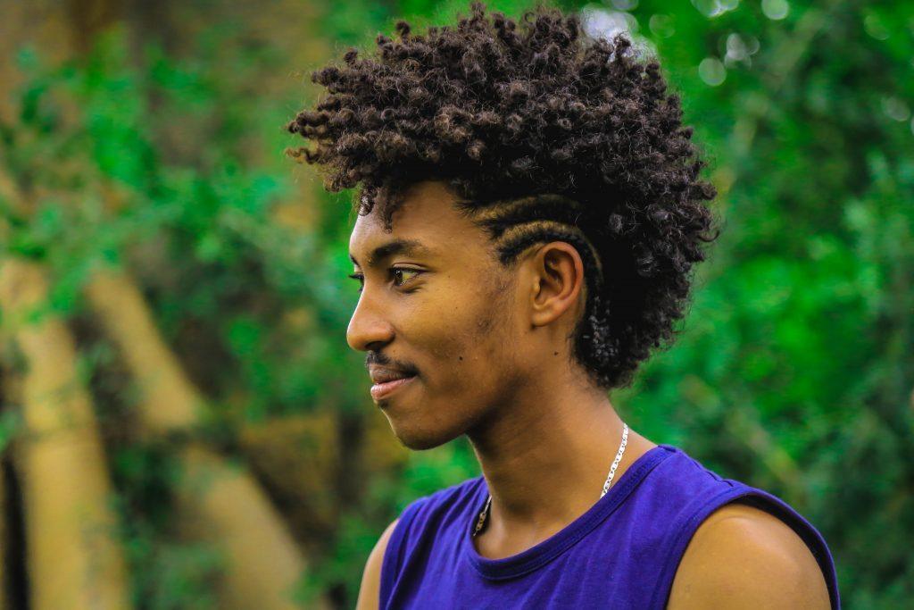 Homem negro de perfil, ao ar livre, com árvores ao fundo