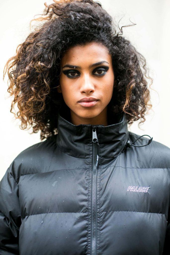 Mulher de cabelo cacheado e jogado de lado usa agasalho preto