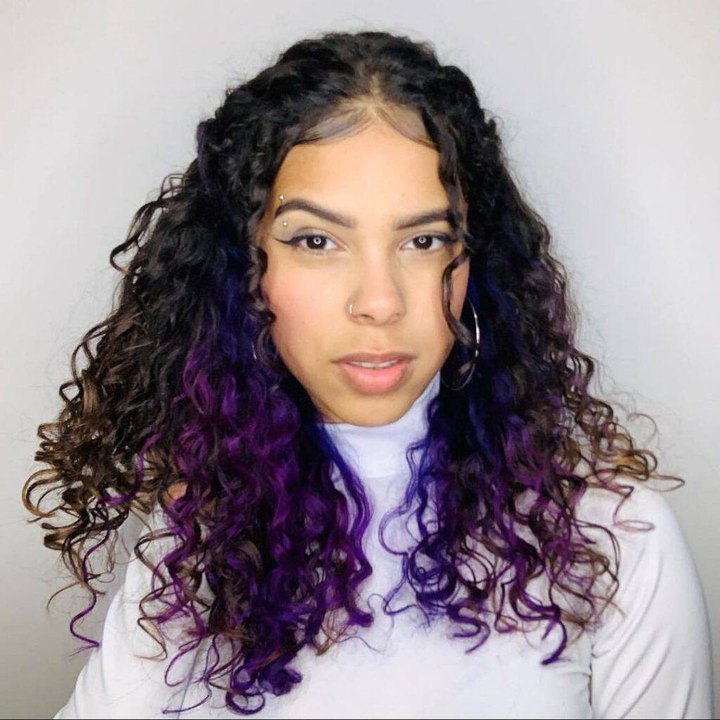 mulher com blusa branca e cabelo cacheado com mechas roxas na nuca