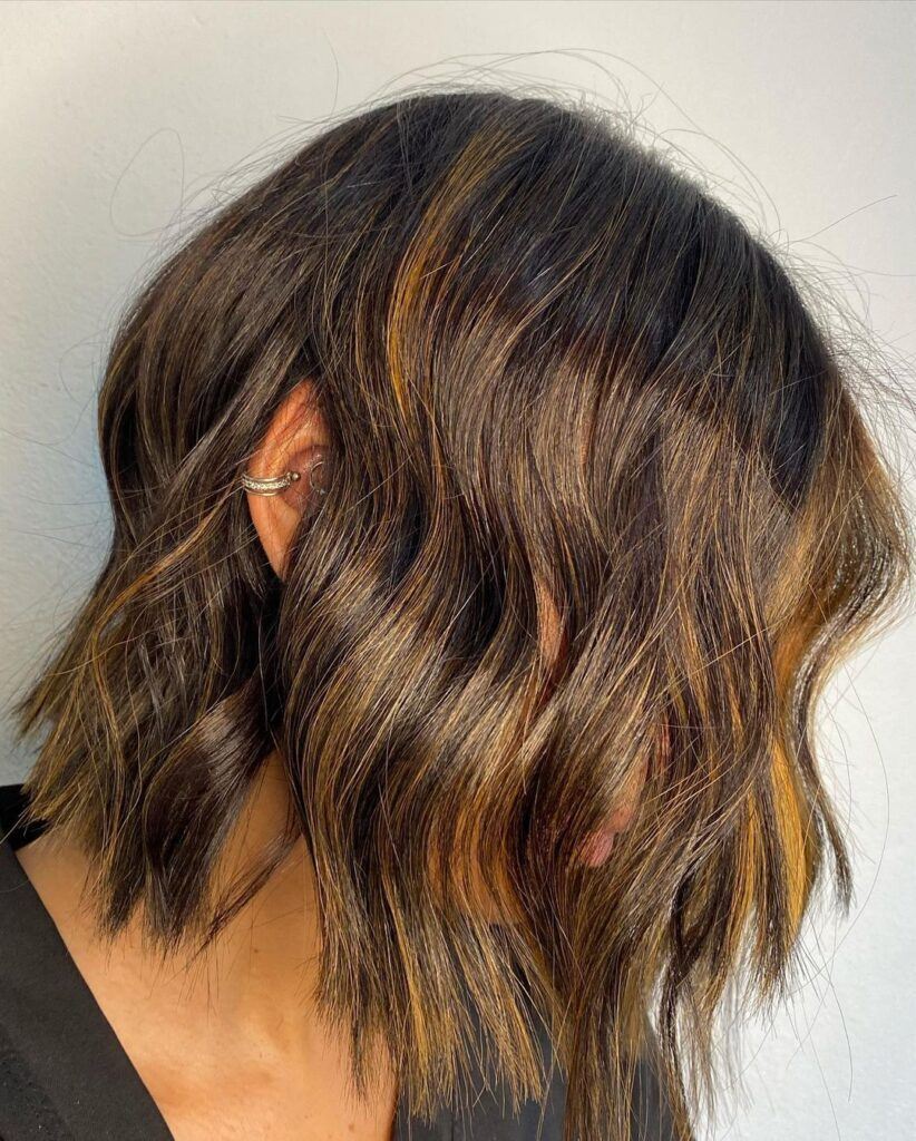 Mulher de perfil no salão com cabelo curto em tons de castanho dourado