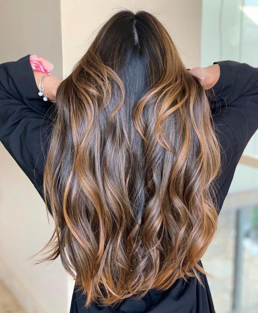 mulher com cabelo castanho iluminado caramelo ondulado longo