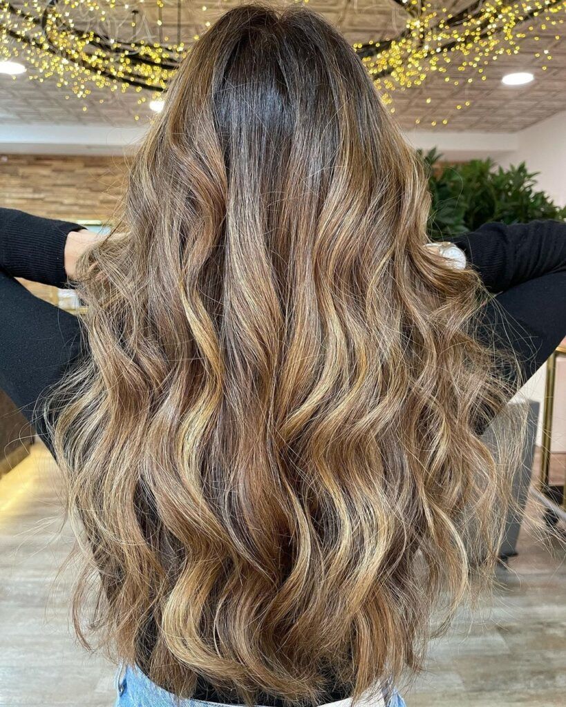 mulher com cabelo castanho iluminado mel ondulado longo