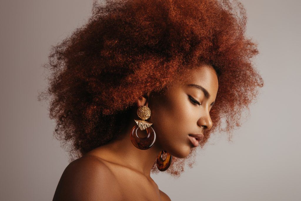 Mulher com cabelo afro ruivo médio e brincos grandes