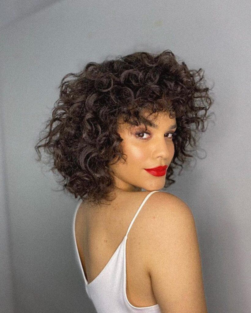 mulher com batom vermelho com cabelo medio cacheado com franja