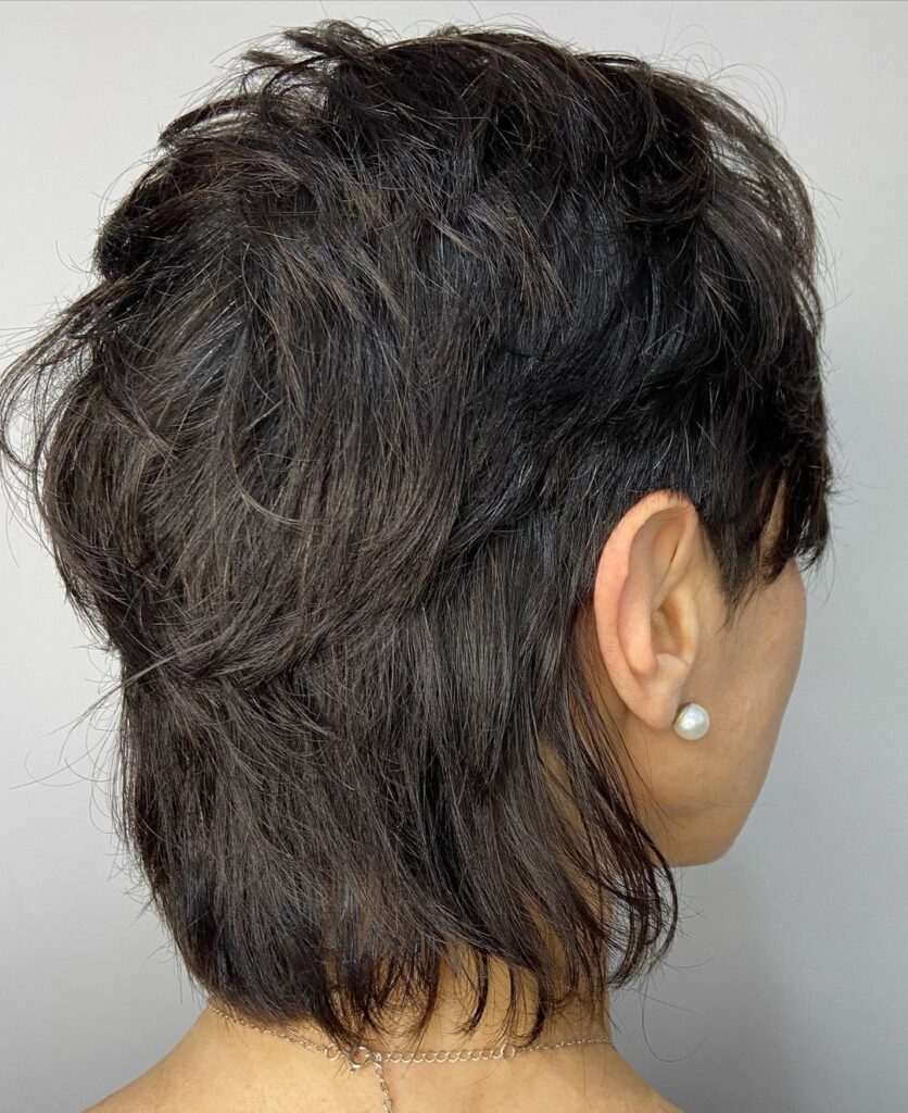 Mulher de costas com brinco na orelha e mullet feminino curto no cabelo preto liso