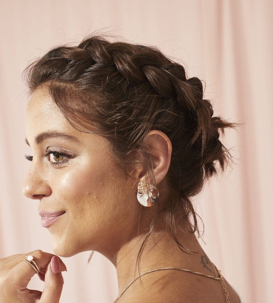mulher de perfil com a mão no queixo enquanto posa com tiara de trança e acessórios