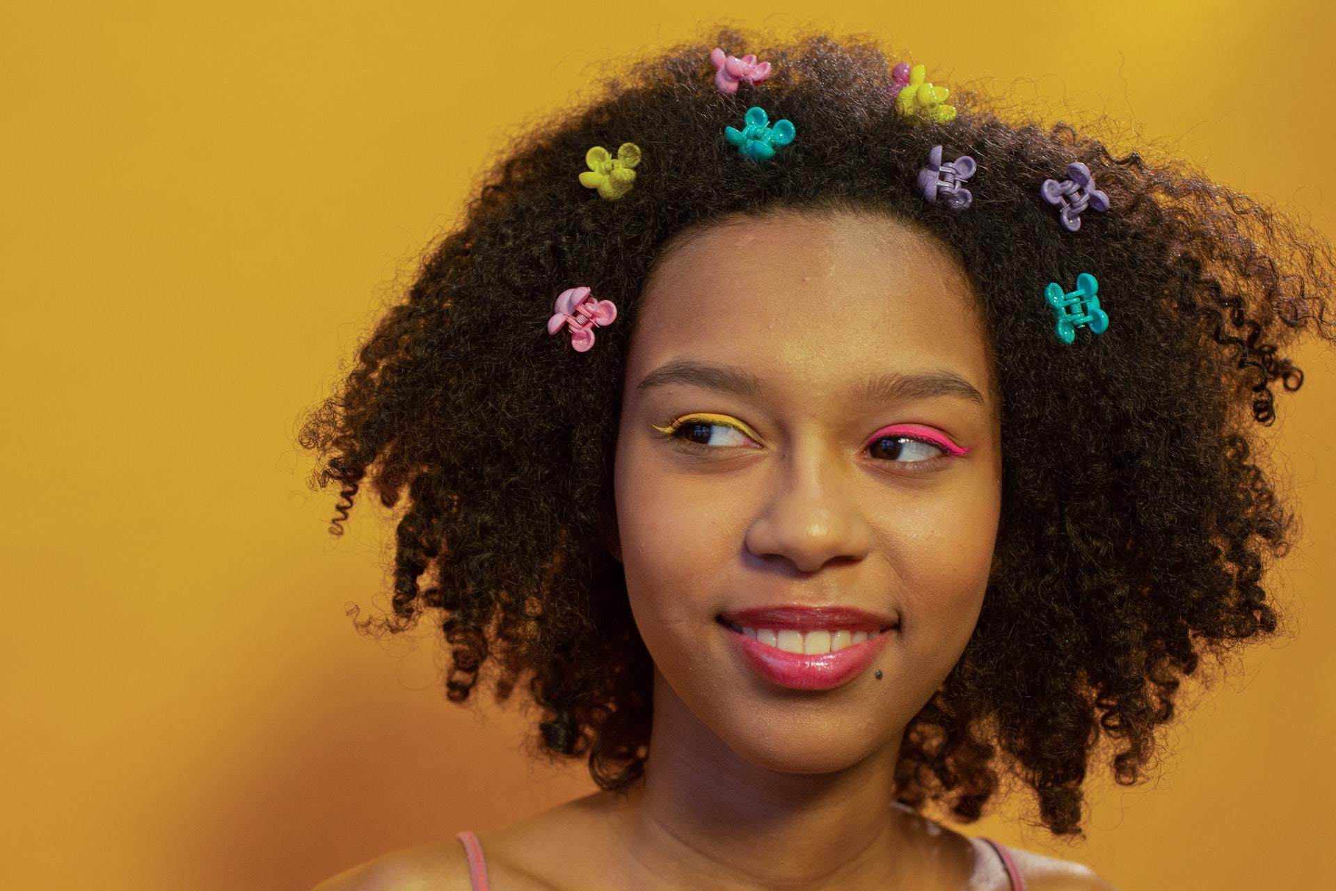 mulher com cabelo crespo e presilhas coloridas de carnaval num fundo amarelo